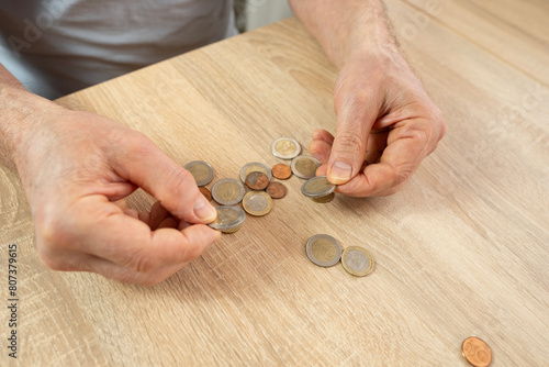Senior man, poor pensioner lays out euro cent coins on wooden table, counts meager cash money on table, illustrating harsh reality life in poverty photo