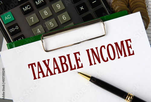 TAXABLE INCOME - words on a white sheet on the background of a calculator and a pen