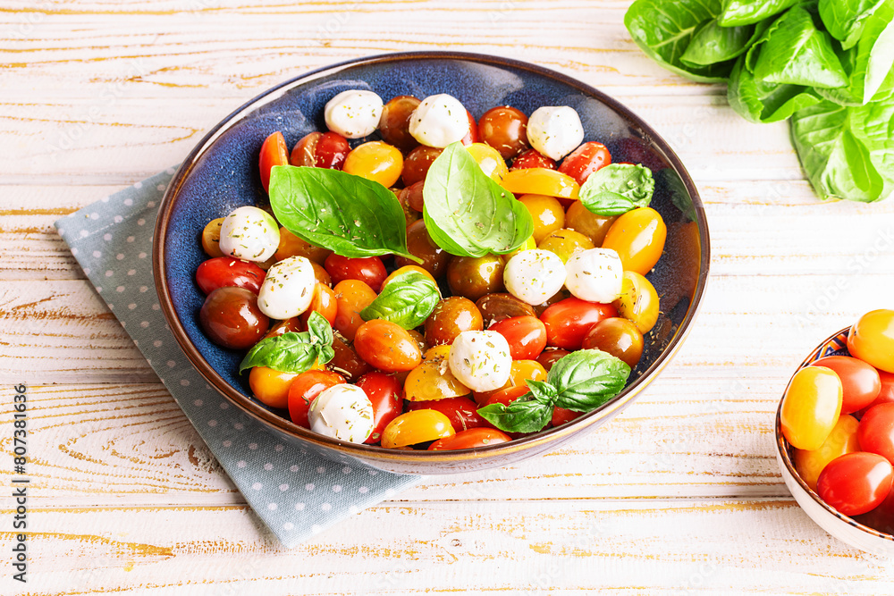 Fresh homemade caprese salad with baby mozzarella cheese, cherry tomatoes, basil leaves and olive oil on rustic wooden table close up. Country style dinner concept. Fresh homemade caprese salad with baby mozzarella cheese, cherry tomatoes, basil leaves and olive oil on rustic wooden table close up. Country style dinner concept.