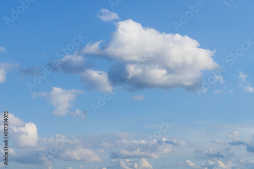 Serene blue sky with a large fluffy cloud in the center and a cluster of other clouds closer to the horizon.