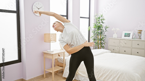 A young blonde woman stretches in a sunlit bedroom adding wellness to her morning routine