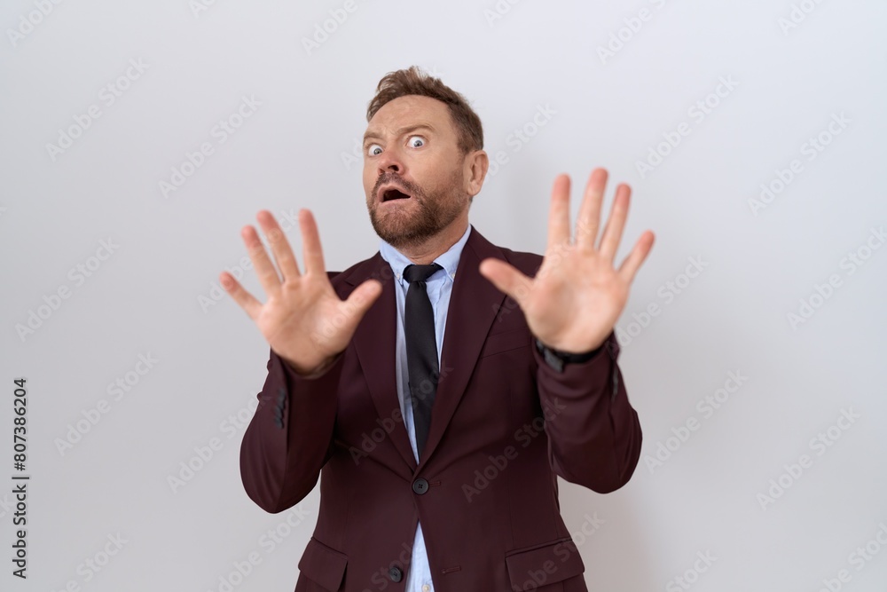 Middle age business man with beard wearing suit and tie afraid and terrified with fear expression stop gesture with hands, shouting in shock. panic concept. Middle age business man with beard wearing suit and tie afraid and terrified with fear expression stop gesture with hands, shouting in shock. panic concept.