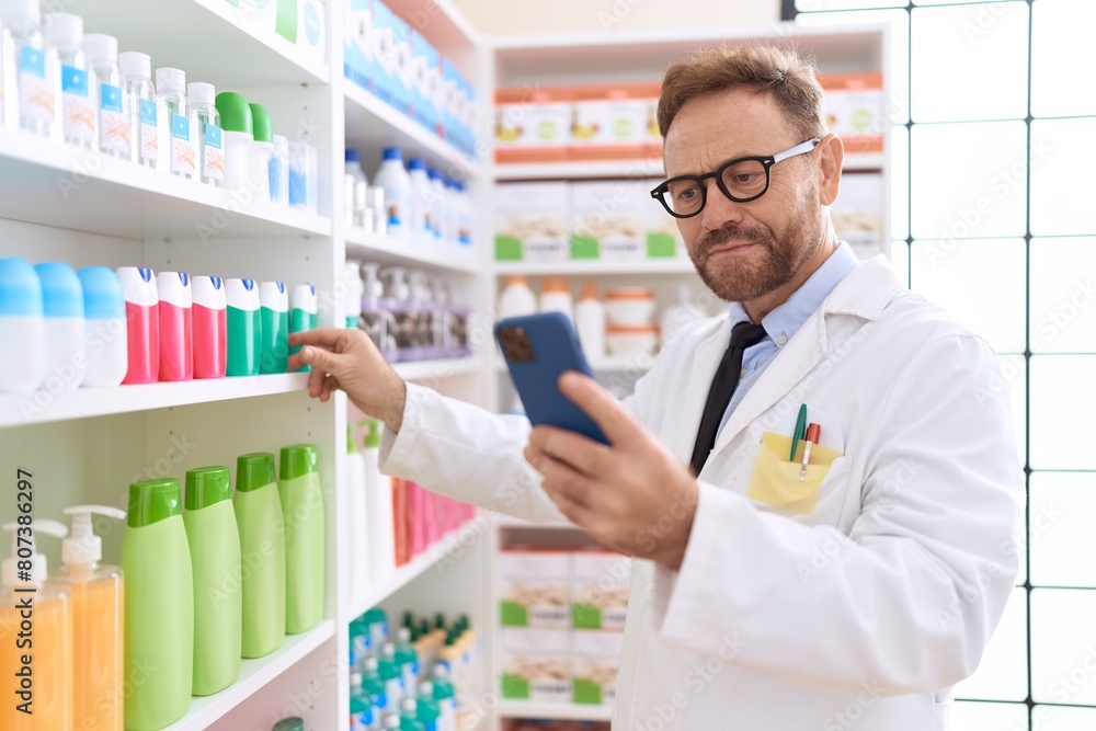 Middle age man pharmacist using smartphone working at pharmacy Middle age man pharmacist using smartphone working at pharmacy