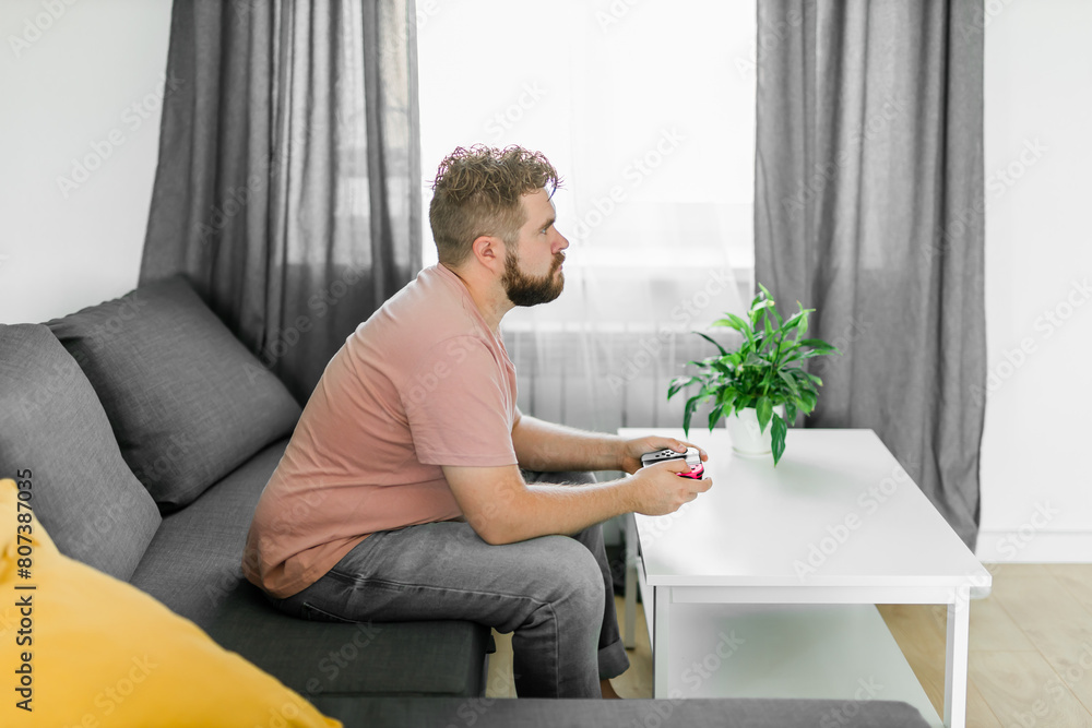 Young man spending time at home, sitting on a couch in apartment and playing arcade car video games on console. Male using controller to play street racing drift simulator. Young man spending time at home, sitting on a couch in apartment and playing arcade car video games on console. Male using controller to play street racing drift simulator.
