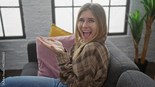 A smiling young woman stretches out palms in a cozy living room with exposed brick and modern decor.