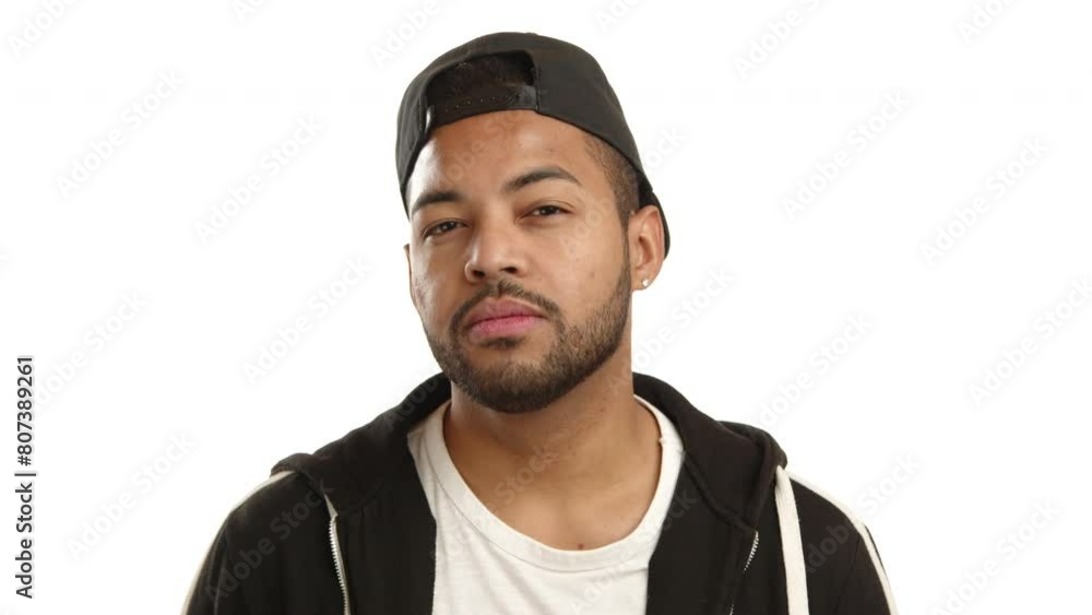 A contemplative mixed-race man with a serious expression and black cap looking intently into the camera on a white background. Camera 8K RAW. A contemplative mixed-race man with a serious expression and black cap looking intently into the camera on a white background. Camera 8K RAW.