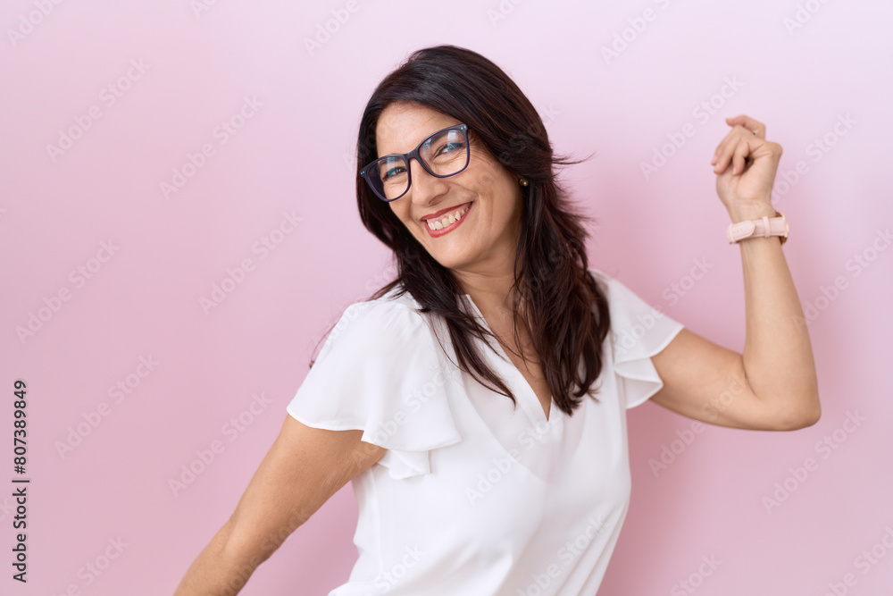 Middle age hispanic woman wearing casual white t shirt and glasses dancing happy and cheerful, smiling moving casual and confident listening to music Middle age hispanic woman wearing casual white t shirt and glasses dancing happy and cheerful, smiling moving casual and confident listening to music