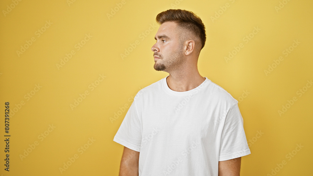 Handsome hispanic man with beard posing in white shirt against yellow wall, showcasing modern casual style. Handsome hispanic man with beard posing in white shirt against yellow wall, showcasing modern casual style.