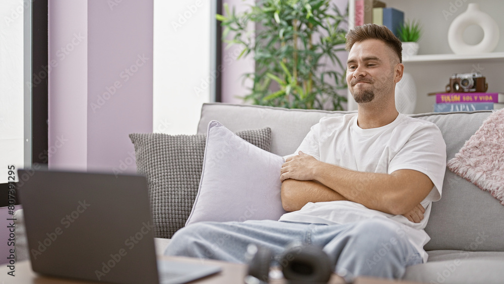 Hispanic man relaxing on couch with laptop and camera in a modern living room Hispanic man relaxing on couch with laptop and camera in a modern living room