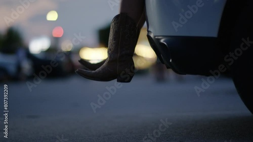 Woman wearing cowboy boots sits in the back of her car while tailgating at a country music concert