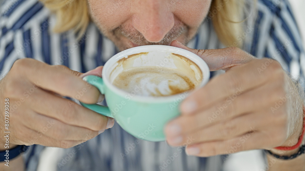Handsome young man with long blond hair enjoying a cappuccino at an outdoor cafe Handsome young man with long blond hair enjoying a cappuccino at an outdoor cafe