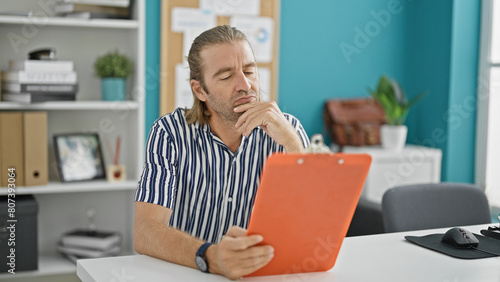 Wallpaper Mural Pensive man with long blond hair contemplating a clipboard in a modern office setting Torontodigital.ca