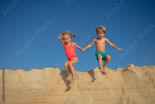 Happy siblings take playful leap from a sand heap on sunlit day