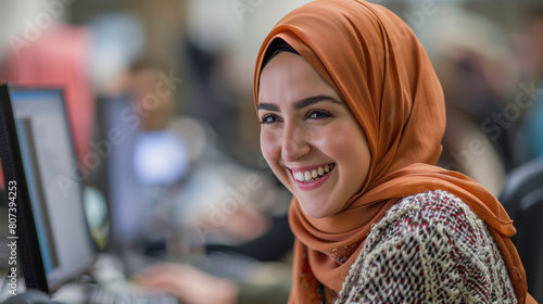 Happy hijabi female socialising with colleagues in office meeting. Candid smiling white muslim woman with headscarf laughing with team & working at computer. Inclusive & diverse workplace © Sophie 