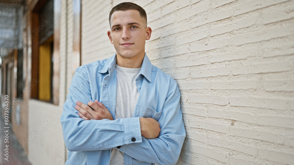 Handsome young hispanic man with crossed arms standing confidently on a city street, portraying casual style. Handsome young hispanic man with crossed arms standing confidently on a city street, portraying casual style.