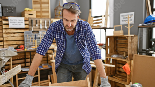A middle-aged hispanic man with a beard works attentively in a carpentry workshop, embodying skilled craftsmanship.