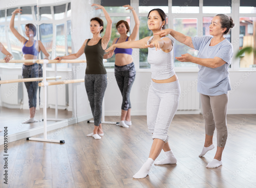 Elderly female trainer helps beginner women perform ballet movements correctly