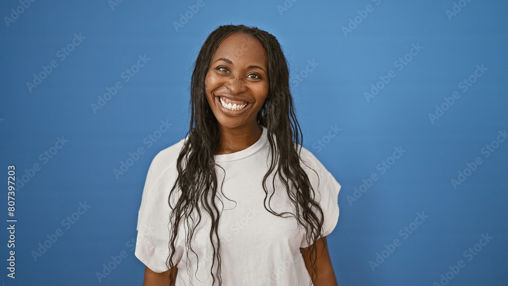 Smiling young adult woman with curly hair against a blue background, evoking happiness and confidence.