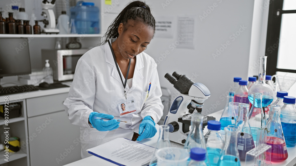 African american female scientist analyzing samples in a laboratory equipped with chemicals and a microscope. African american female scientist analyzing samples in a laboratory equipped with chemicals and a microscope.