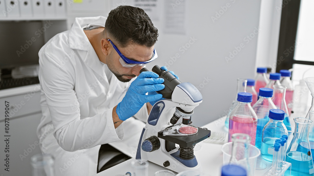 A young man examines a specimen under a microscope in a laboratory setting, surrounded by scientific equipment. A young man examines a specimen under a microscope in a laboratory setting, surrounded by scientific equipment.