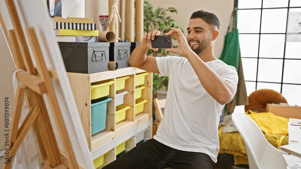 A handsome man capturing photo of his artwork with a smartphone in a creative indoor studio setting. A handsome man capturing photo of his artwork with a smartphone in a creative indoor studio setting.