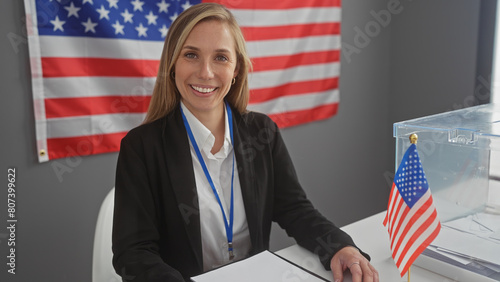 A smiling woman with a badge stands by a ballot box in a room with the american flag, symbolizing democracy and civic duty. photo