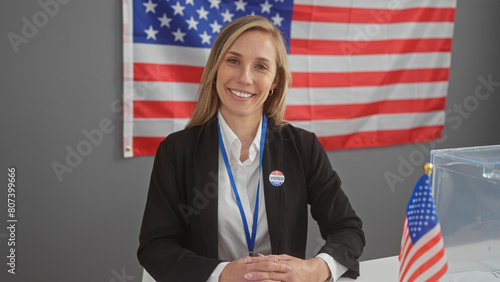 Smiling woman with a 'voted' sticker, american flag backdrop in a voting center.
