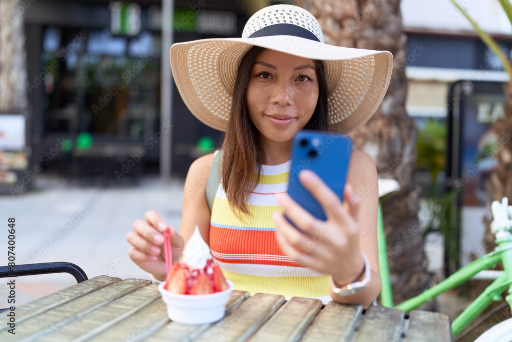 Young asian woman tourist eating ice cream using smartphone at coffee shop terrace