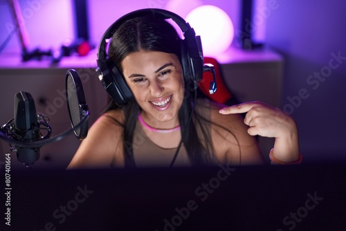 Young hispanic woman playing video games wearing headphones smiling happy pointing with hand and finger photo