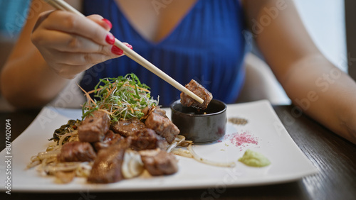 Young woman joyfully digs into her delicious gourmet beef meal, heartily using her chopsticks at a modern asian restaurant. she's enjoying her fresh japanese cuisine for an amazing lunch or dinner