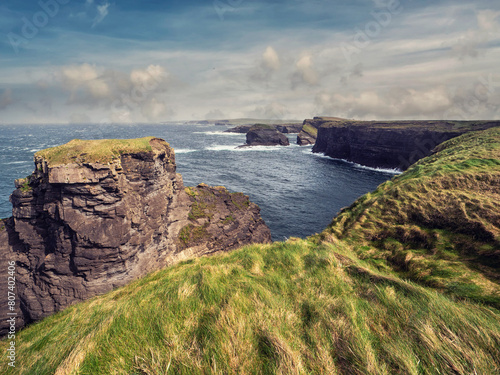 Kilkee cliff in county Clare, Ireland. Popular travel area with stunning nature scenery with green fields, ocean and dramatic sky. Irish landscape. Rough coast line. Warm sunny day.