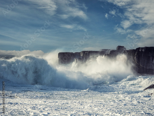Powerful tall ocean wave hit stone cliff and create huge splash of water. County Clare, Ireland. Storm weather. Rough sea. Power of nature. Irish landscape scene. Cloudy sky. © mark_gusev