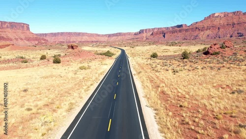 Empty intercity highway with black asphalt and yellow road markings pass through hot dry desert in western usa background of red rock massive butte in colorado river canyon. Aerial flying. Road trip