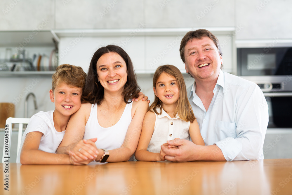 Fototapeta premium Joyful family with two children posing at dinner table in kitchen at home