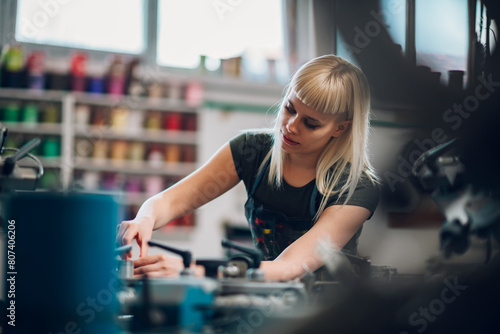 Printing shop worker manipulating screen printing press at factory.