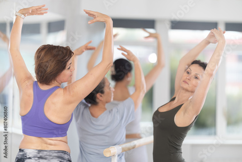 Adult female teacher showing ballet moves to group of beginner women in studio