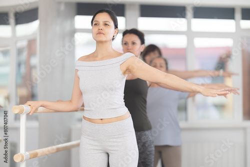 Group of female beginners practicing second ballet position at barre in dance studio photo
