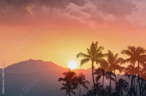 Beautiful tropical sunset with palm trees and golden sun setting over the mountains top
