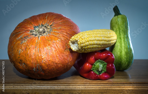 Some colorful vegetables on wooden table, orange squash, zucchini, red pepper and corn. Hard lighting