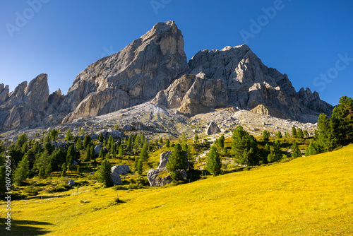 Picturesque mountain landscape overlooking rocky pinnacles of Munt de Fornella framed by greenery of sprawling alpine meadow on sunny summer day. Enchanting nature of Dolomites, Italy photo