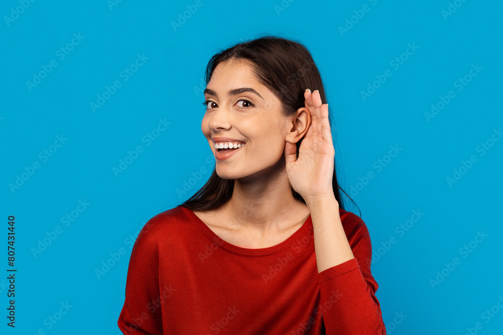 A woman with a joyful expression on her face is smiling and touching her ear with her hand, indicating she might be listening or adjusting an earpiece. She appears content and engaged in the moment. A woman with a joyful expression on her face is smiling and touching her ear with her hand, indicating she might be listening or adjusting an earpiece. She appears content and engaged in the moment.