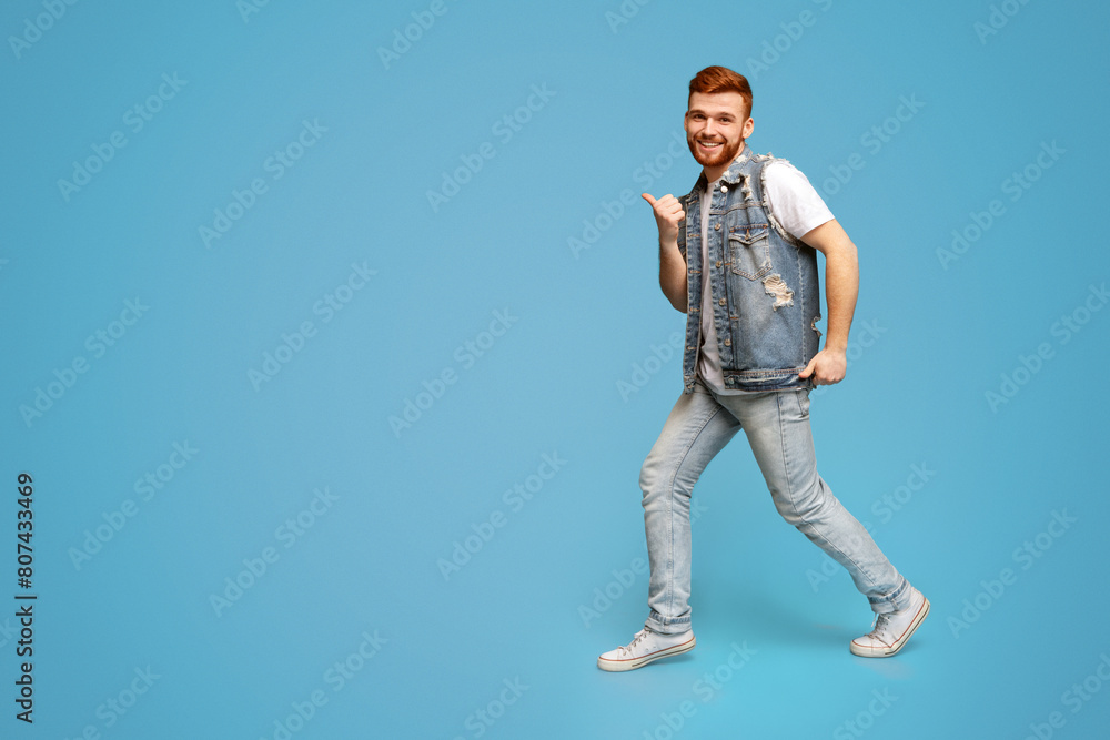 Naklejka premium Cool millennial man dancing with thumbs up gestures on blue background, studio, copy space