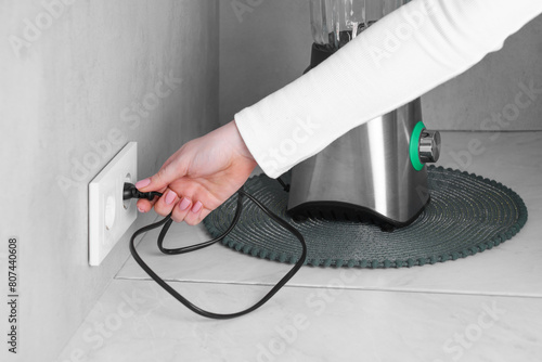 Fotografie Woman plugging blender into socket at white table indoors, closeup