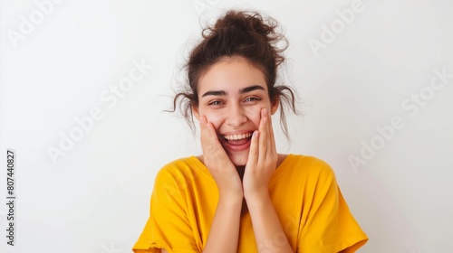 Young woman in yellow t-shirt laughing with hands on face against white background. photo