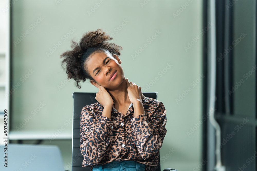 A young African American woman with Afro brown hair in a modern office experiencing office syndrome, including pain, stress, tiredness, and various physical and mental health issues.