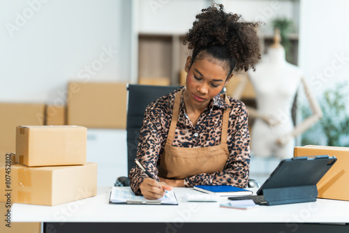 Φωτογραφία A young African American woman with afro brown hair works in a modern office, managing her small business, utilizing laptop technology for e-commerce, shipping, and marketing, sme box