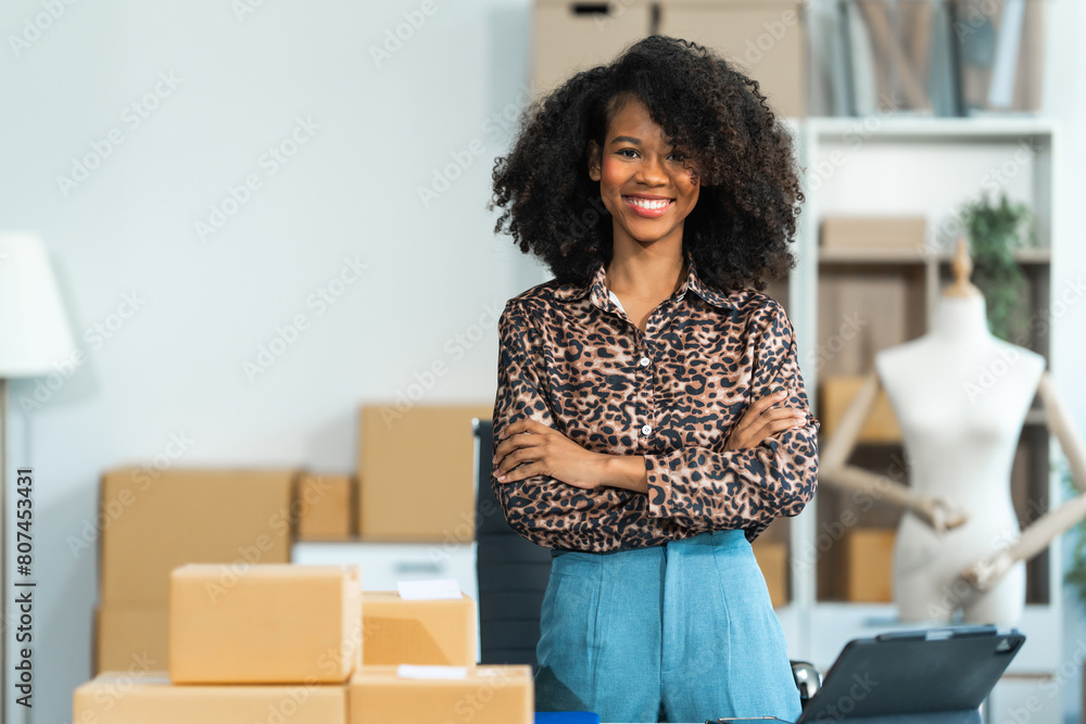 A young African American woman with afro brown hair works in a modern office, managing her online clothing store and live stream platform, sme box packages. A young African American woman with afro brown hair works in a modern office, managing her online clothing store and live stream platform, sme box packages.