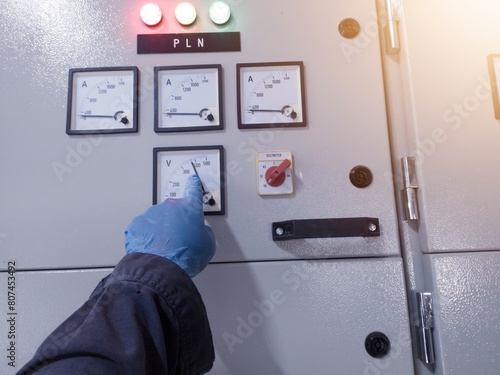 An engineer wearing blue gloves shows the working voltage value on the main control panel, the concept of inspection and checking work.