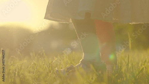 Kid step. Child feet walk along green lawn in park in spring. Legs of little girl walk along green grass in rays of sun, closeup. Happy family with child on walk in summer park. Baby walking on grass. photo