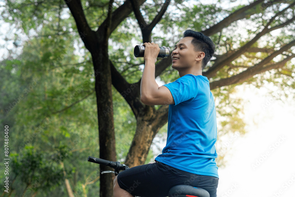 Asian Man Cycling in Blue Sports Shirt, Holding bottle or Drinking from Bottle concept. Healthy and sporty advertising concept Asian Man Cycling in Blue Sports Shirt, Holding bottle or Drinking from Bottle concept. Healthy and sporty advertising concept